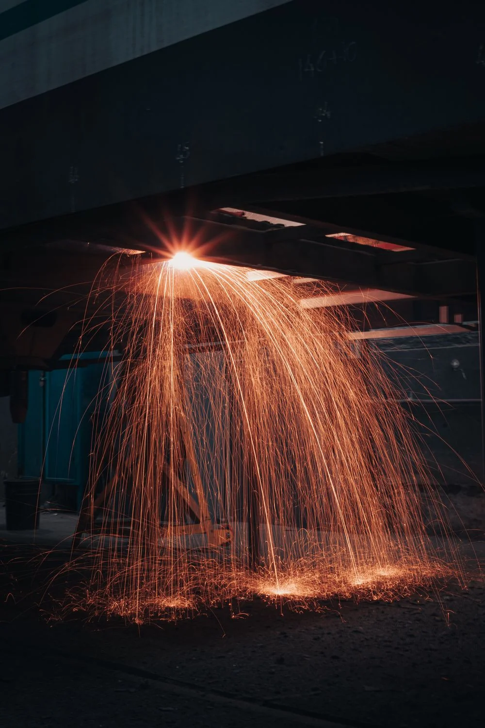 Fabrika atölyesinde metal kesimi sırasında aşağı yayılan turuncu kıvılcımlar